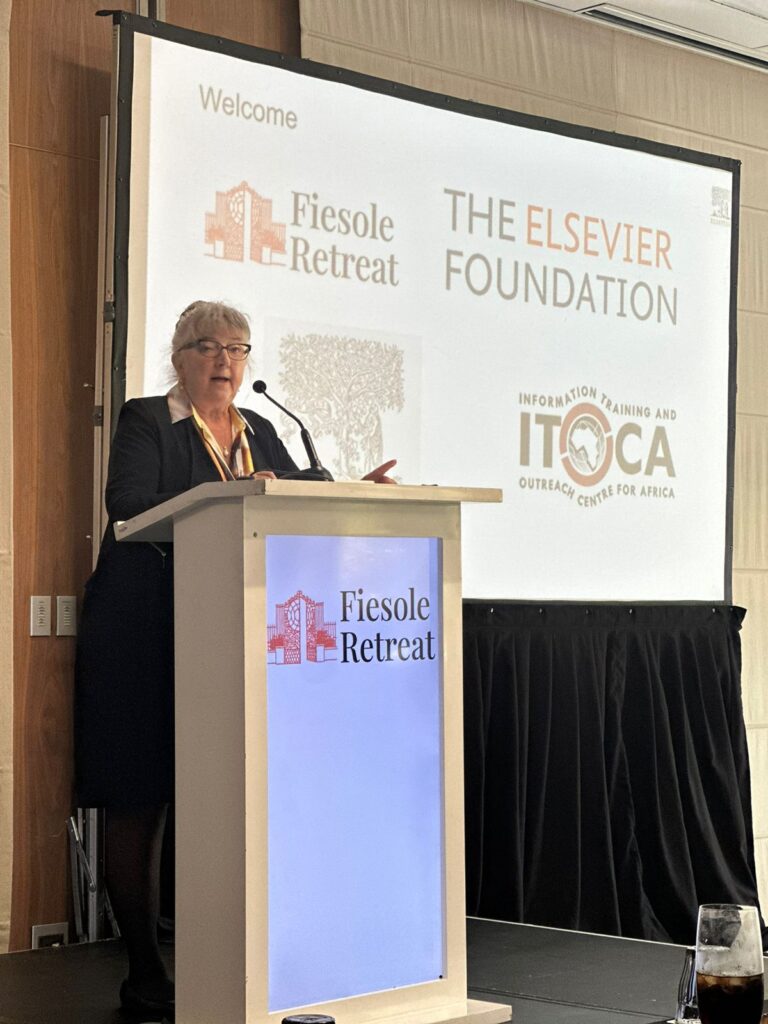 Speaker at a podium presenting at the Fiesole Retreat with a screen displaying ‘The Elsevier Foundation’ and ‘ITOCA Outreach Centre for Africa.’