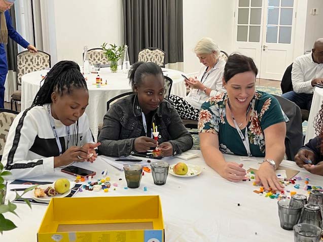 Participants seated at a table during a workshop, building models with small colorful blocks and smiling while working together.